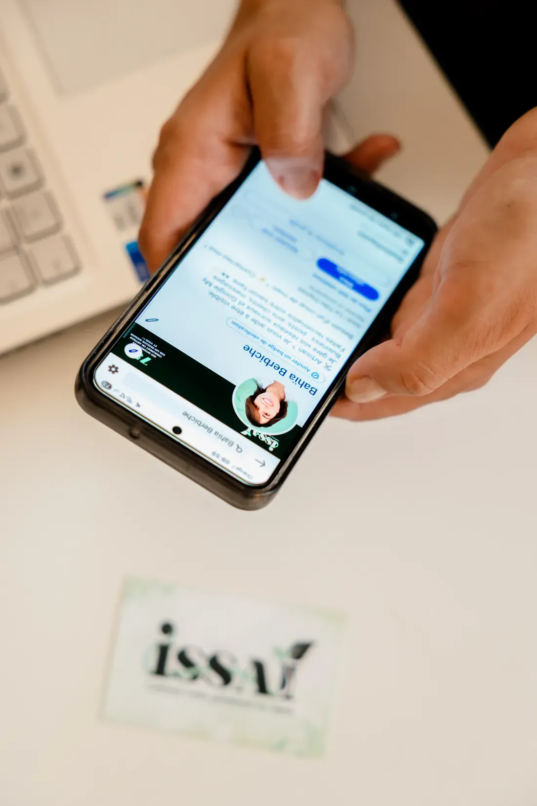 Bahia, fondatrice d’ISSAÏ, consulte un profil réseaux sociaux sur son téléphone, carte ISSAÏ posée sur le bureau